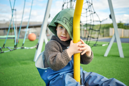 Little boy hanging on swing on playground