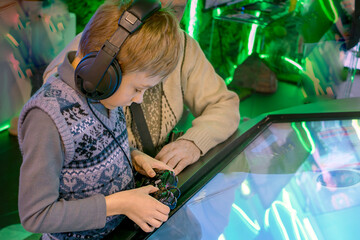 Boy wearing headphones and holding gamepad with his father explores technology on an interactive screen