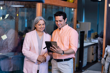 Shot of a two confident business persons talking in the work place. Two colleagues using a digital tablet while walking in a modern office