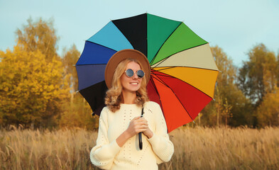 Happy young woman with colorful umbrella in autumn park, enjoys warm weather, fall season background