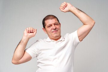 Fototapeta premium Happy older man showing off his strong biceps while standing against a light gray background