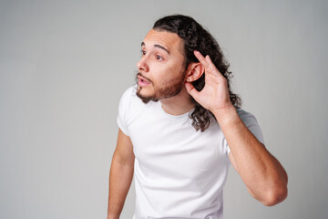 A young man with curly hair listening attentively while standing against a plain background