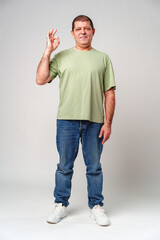 A man with a slight smile making an OK hand gesture against a neutral background