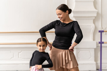 Fototapeta premium Winsome woman and little girl practicing ballet together in hall learning dancing