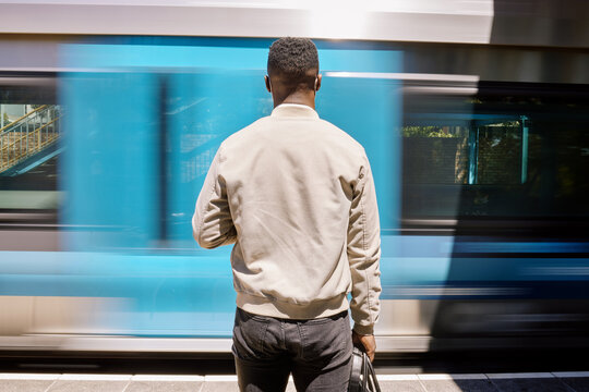 Business, black man and train with luggage for commute, urban travel and morning journey of metro transport. Male person, back and suitcase with waiting , railway station and platform departure