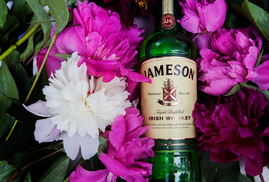 Lviv / Ukraine - 06.09.2020: A large bottle of Irish whiskey Jameson 700 ml lies on a white wooden table on spring-summer flowers, with space for text, without anyone