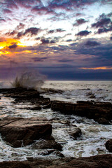 Fototapeta premium A symphony of nature unfolds as the waves crash against the rocks, accompanied by the golden light piercing through the clouds.