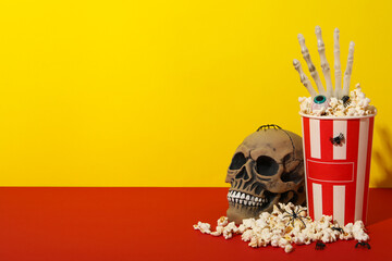 Paper cup of popcorn and Halloween decorations on yellow background, space for text