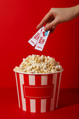 Large paper cup of popcorn and movie tickets in hand on red background