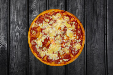 Italian pepperoni pizza with sausage and cheese, top view, on black wooden background.