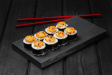 Japanese sushi, rolls baked with sauce on black wooden background.