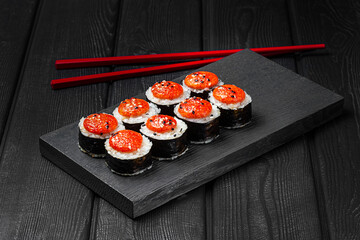 Japanese sushi, rolls baked with sauce on black wooden background.