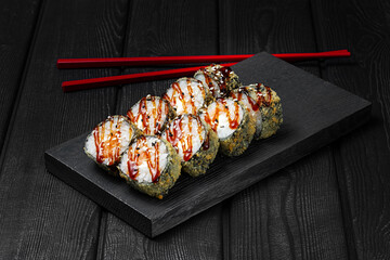 Japanese sushi, rolls fried with salmon and teriyaki sauce on a black wooden background. Tempura...