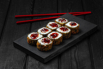 Japanese sushi, rolls fried with teriyaki sauce on black wooden background. Tempura roll