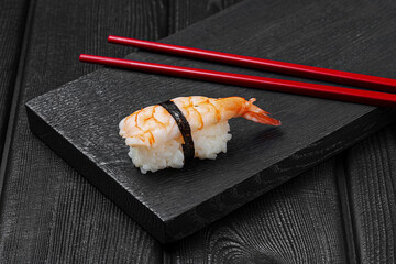 Japanese nigiri sushi with shrimp on black wooden background.
