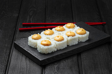 Japanese sushi rolls with cheese sauce on top on black wooden background. 