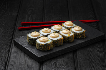 Japanese sushi, rolls fried with mushroom sauce on top on black wooden background. Tempura roll