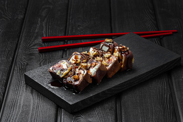 Japanese sushi, sweet rolls with nuts and chocolate topping on a black wooden background.