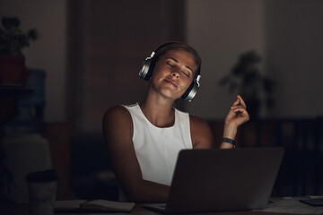 Woman, headphones and laptop with music in office at night for work break, listening to radio or...