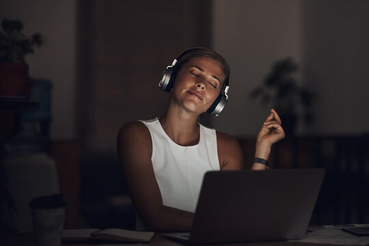 Woman, headphones and laptop with music in office at night for work break, listening to radio or audio playlist. Small business, employee and person dancing to favorite song at workplace with relax