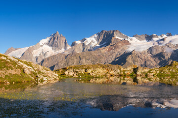 Lerie Lake in the Oisans Massif with scenic view of La Meije peak in Ecrins National Park at sunset. GR 54 hiking trail on Emparis Plateau. Hautes-Alpes, Alps, France
