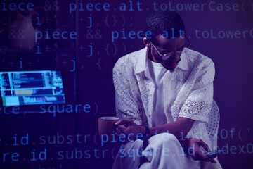 Professional black person engrossed with coding on computer while using smartphone in contemporary...