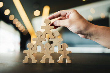 A model of people arranged in the shape of a pyramid with an executive's hand picking up the model...