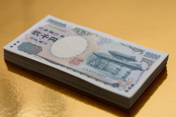 Stack of 2000 yen bills neatly placed on a golden surface highlighting the intricate design of the...
