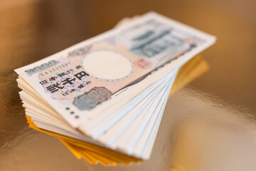 Stack of 2000 yen bills fanned out on a golden surface with selective focus, highlighting currency...