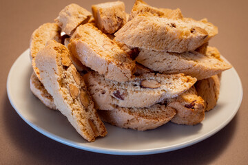 A plate of Italian almond cantucci cookies piled on a brown surface The golden-brown biscotti with visible almond pieces highlight their crunchy texture and nutty flavor