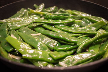 Flat Italian green beans are being sauteed in a pan with garlic and spices The bright green beans glisten with oil as they are cooked to serve as a flavorful side dish
