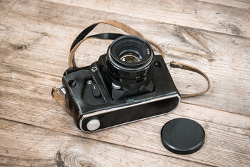 Black Soviet film camera in a leather case on a wooden unpainted surface with knots