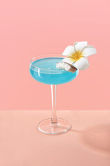 Blue margarita cocktail with floral garnish. Tropical drink on coral background. Copy space
