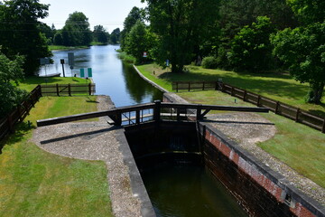 View of a wooden dam or sluice with massive gates and walls covered with stone and red bricks located next to a vast forest or moor and allowing to keep the proper water level seen in summer in Poland