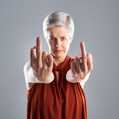 Hand gesture, portrait and rude with senior woman in studio on gray background for disrespect. Anger, emoji and obscene with unhappy mature person showing middle finger for conflict or protest