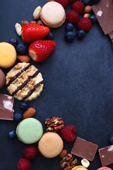 Macarons, chocolate, cookies, berries and various nuts on dark blue background. Top view.