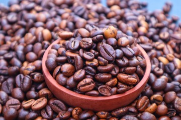Fototapeta premium Robusta coffee beans or Coffea canephora in a wooden bowl and on top of a pile of coffee beans around it, close up view.