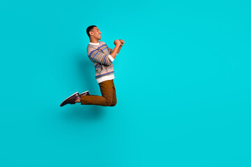 Full size photo of nice young man raise fists jump empty space wear sweater isolated on teal color background