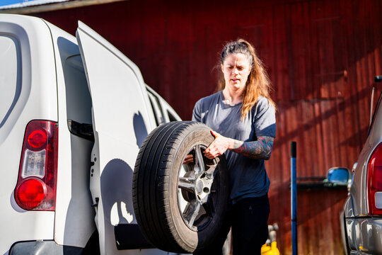 Female repairperson removing tire from mini van at sunny day