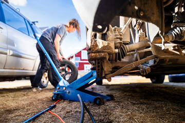 Vehicle lifted by car jack while female mechanic standing with tire on sunny day