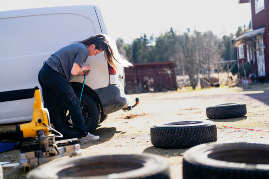Focused female repairperson fastening nut of car tire using lug wrench at sunny day