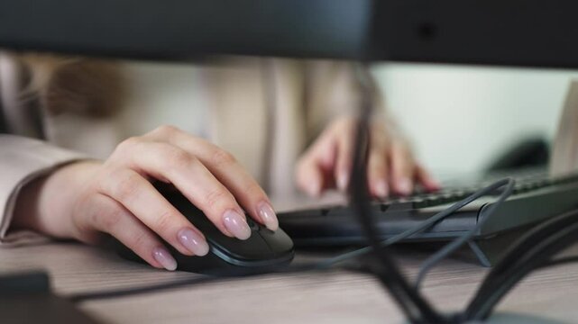 Woman with light-colored manicure works at computer. Female analyst attentively enters data into program using keyboard and mouse