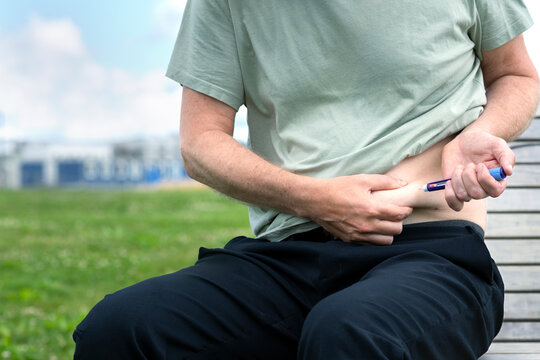 Midsection of man injecting diabetes insulin while sitting on bench at park
