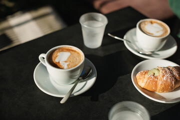 Close-up of cappuccino, glasses of water and croissant with pistachio cream on a table.