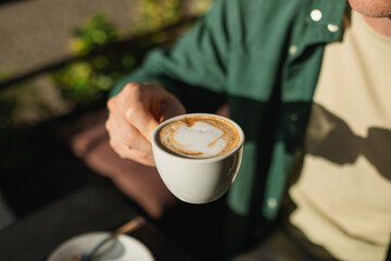 Overhead view of a man sitting at an outdoor cafe drinking a delicious cappuccino on a sunny morning.