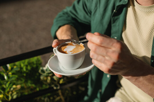 Close-up of a man sitting at an outdoor cafe drinking a cappuccino on a sunny morning.