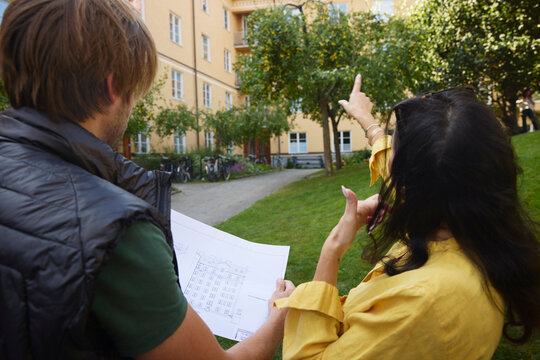 Rear view of female architect pointing while male colleague examining blueprint in garden