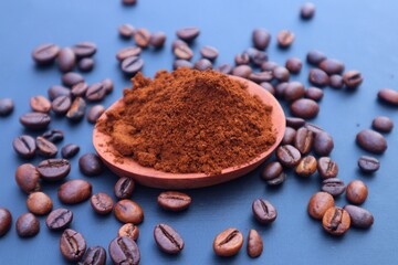 Robusta coffee grounds or Coffea canephora in a wooden bowl and Robusta coffee beans scattered around it. Close-up view, with dark background.
