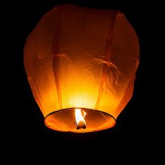 A single sky lantern isolated on black background. Rising in the dark night sky. single light in the darkness