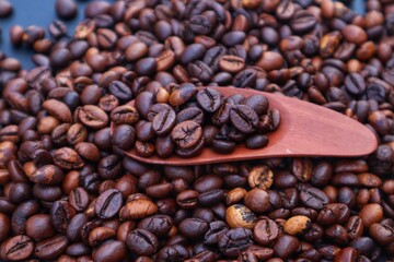 Robusta coffee beans or Coffea canephora in a wooden spoon on a pile of coffee beans, close up view.
